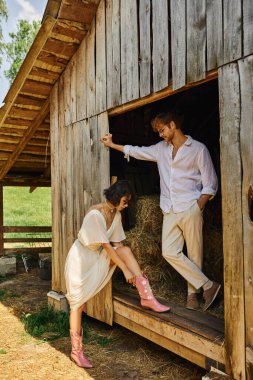 stylish asian bride wearing pink cowboy boots near redhead groom while standing near wooden barn clipart