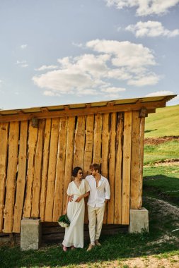 Boho tarzında kırsal bir düğün, gelinlik giymiş Asyalı gelin ve damatla birlikte duran kovboy çizmeleri.