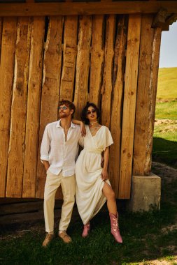 Boho tarzında kırsal bir düğün, şık bir Asyalı gelinlik içinde damat ve güneş gözlüklü bir gelin.