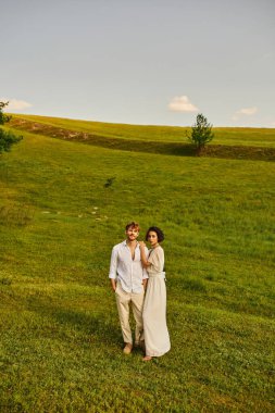 Daha yeni evlenmiş çok kültürlü bir çift yeşil alanda, manzaralı ve huzurlu bir arazide yan yana duruyor.