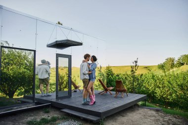 Modern cam evin yakınındaki verandada kucaklaşan genç çift, kırsalda romantik bir randevu.