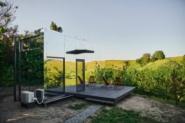 Verandasında sandalye ve sehpa olan modern minimalist cam ev, huzur ve manzaralı.
