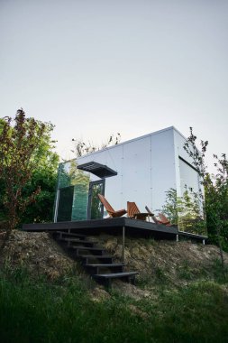 Ahşap merdivenleri ve verandası olan modern çevre dostu cam ev, sakin kırsal alan.