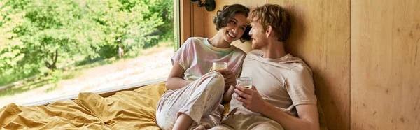 幸せな異人種間のカップルは ベッドに座って カントリーハウスで朝のコーヒーのカップを保持しています バナー — ストック写真