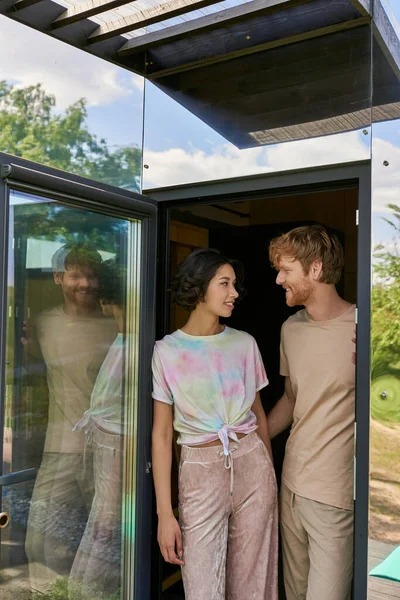 stock image happy asian woman looking at redhead boyfriend while leaving home, standing near entrance together