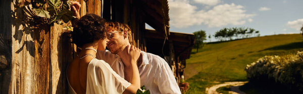 мужчина в солнцезащитных очках, держащий букет и флиртующий с азиатской невестой в свадебном платье возле сарая, баннер