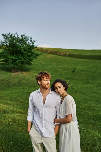 bond between couple, young interracial newlyweds standing in green field, scenic landscape
