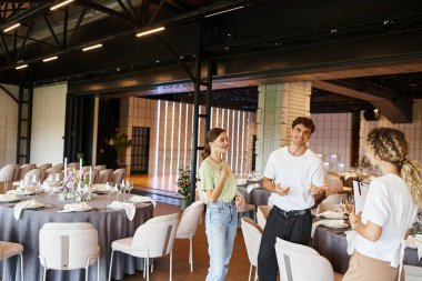 Güler yüzlü etkinlik yöneticilerinden oluşan yaratıcı ekip şölen salonunda masaların yanında şenlik ortamı ile konuşuyorlar.