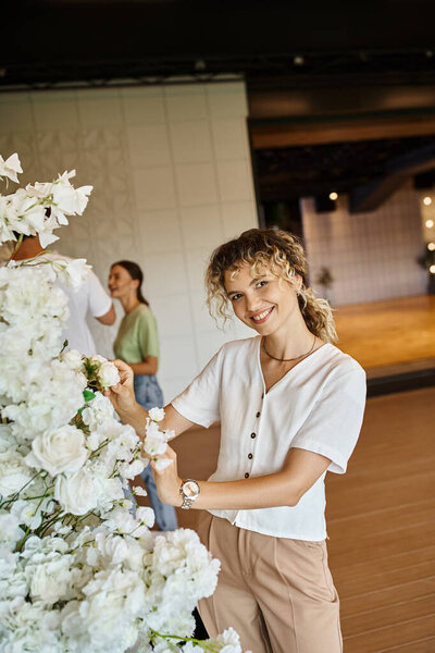 team of creative decorators arranging floral decor in modern spacious event hall, festive design