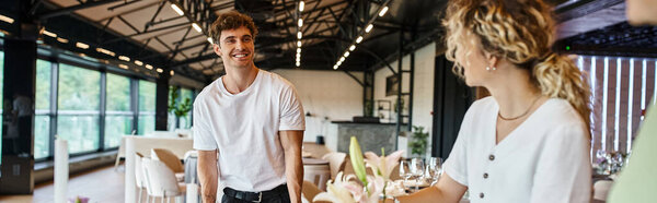 декоратор улыбается коллегам с цветами у стола с праздничной обстановкой в зале мероприятий, баннер