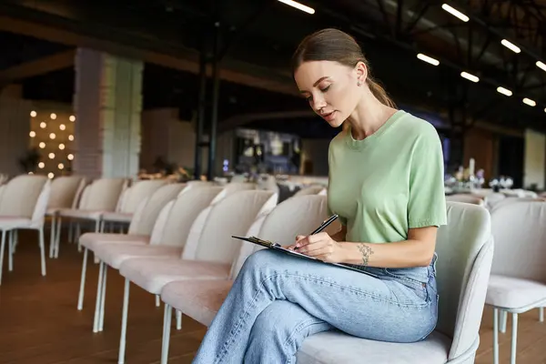 stock image concentrated event manager making notes on clipboard while sitting in armchair in banquet hall