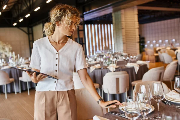 stock image banquet coordinator with clipboard checking festive setting on table in banquet hall, event setup