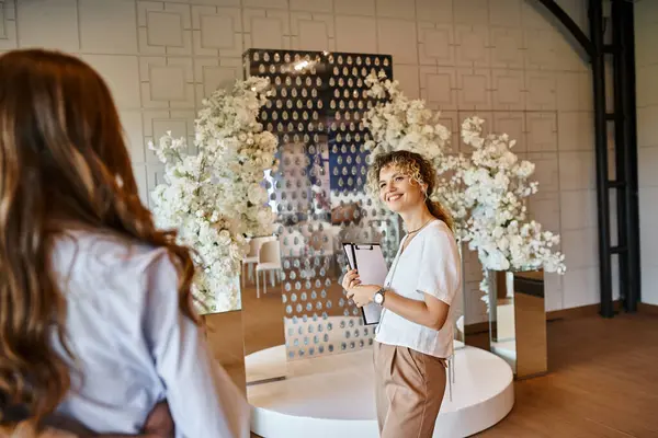Glimlachende Decorateur Met Klembord Tonen Witte Bloemen Decor Aan Geëmailleerd — Stockfoto