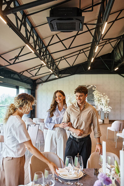banquet coordinator showing decorated festive table to happy couple in event hall, special occasion