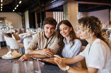 wedding organizer showing contract to smiling couple while sitting at festive table in event hall clipart