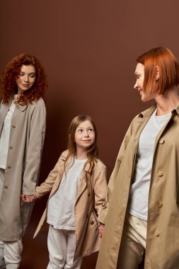 Üç nesildir, paltolu mutlu kızıl aile kahverengi arka planda el ele tutuşuyor, kadınlar ve kızlar.