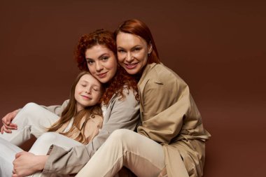 Üç nesil kadın, pozitif kızıl aile kahverengi arka planda kameraya bakıyor, sonbaharda.