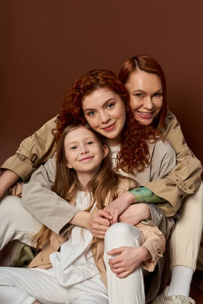 three generations, positive redhead family with freckles looking at camera on brown background