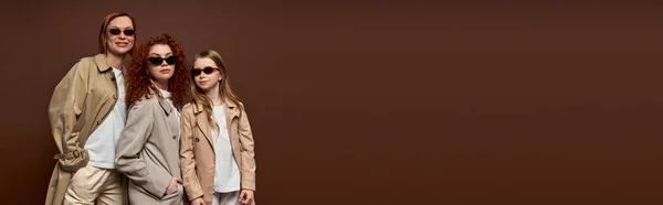 stock image female generations, women and kid with red hair posing in sunglasses and coats on brown, banner
