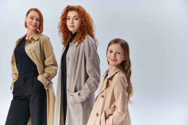 Üç kuşaktır elleri gri ceplerinde poz veren şık ceketli mutlu kızıl saçlı bir aile.