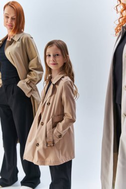 girl in coat posing with hands in pockets near redhead family, three generations of women concept clipart