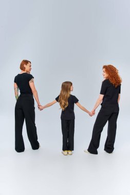 female generations, happy redhead family holding hands and standing in matching attire on grey clipart
