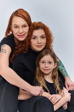 three generations concept, cheerful redhead family in matching outfits hugging on grey backdrop clipart