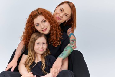 Eşleşen giysiler içinde mutlu bir kızıl aile. Gri arka planda birbirlerine sarılıyorlar. Üç nesildir.