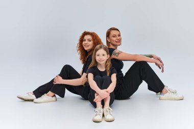 Gri arka planda oturan eşleşen elbiseli kızıl saçlı aile, üç kadın jenerasyon.