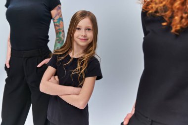 redhead girl standing near women in matching clothes on grey backdrop, three female generations clipart