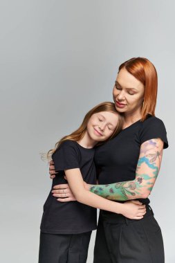 two generations, redhead woman and girl in matching attire hugging on grey backdrop, family love clipart