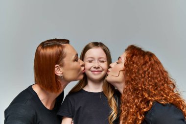 female generations concept, redhead women kissing smiling cheeks of girl on grey background clipart