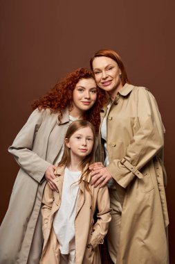 Üç nesil, neşeli kadınlar ve kız Gri arka planda sonbahar trençkotlarıyla poz veriyorlar, moda