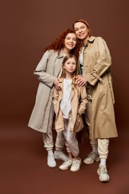 Üç kuşak, mutlu kızıl aile Gri arka planda sonbahar trençkotlarıyla poz veriyor, moda