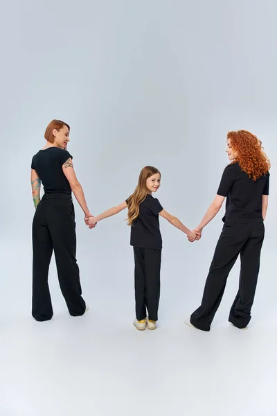 stock image three generations, happy redhead family holding hands and standing in matching attire on grey
