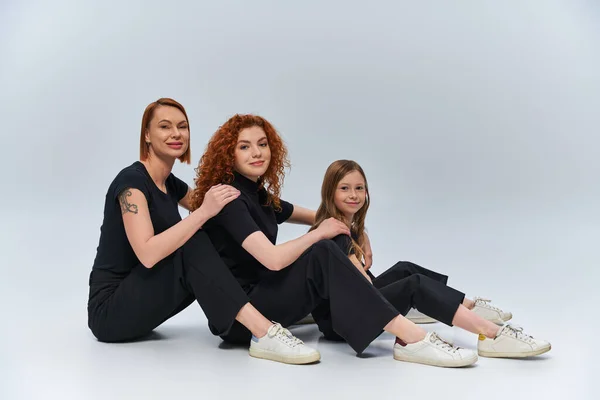 three generations concept, cheerful redhead family sitting in matching outfits on grey backdrop