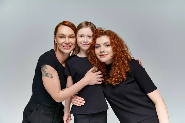 family portrait, redhead women and freckled girl in matching attire smiling on grey background