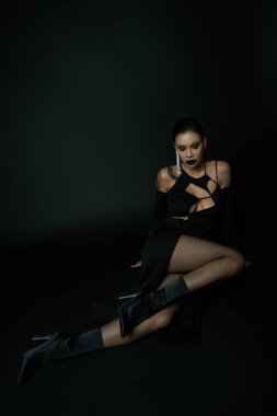 Cadılar Bayramı elbisesi ve koyu makyajlı büyüleyici kadın siyah, gotik cazibesinin üzerinde oturuyor.