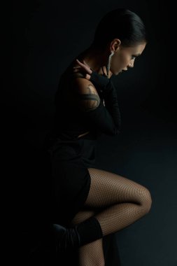 Siyah, siyah güzellikte oturan seksi elbiseli ve balıkçı ağlı taytlı çekici kadının yan görünüşü