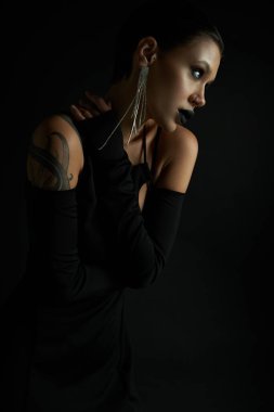 portrait of seductive tattooed woman in stylish and sexy halloween dress looking away on black clipart
