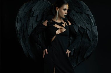 woman in dark makeup and fantasy costume of demonic winged creature looking away on black clipart