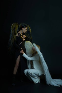 heavenly angel holding hand of dark demon standing on black backdrop, women in Halloween costumes clipart