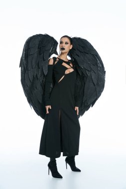 Tam boy esrarengiz kadın kostümü içinde siyah kanatlı şeytan beyaz arka plana bakıyor.