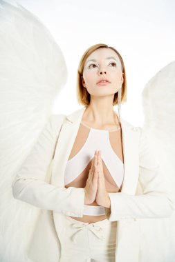 Melek gibi yüzü ve açık kanatları olan bir kadın başka tarafa bakıyor ve beyaz arka planda dua ediyor.