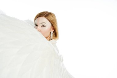 angelic woman looking at camera behind heavenly wings on white backdrop, ethereal beauty clipart