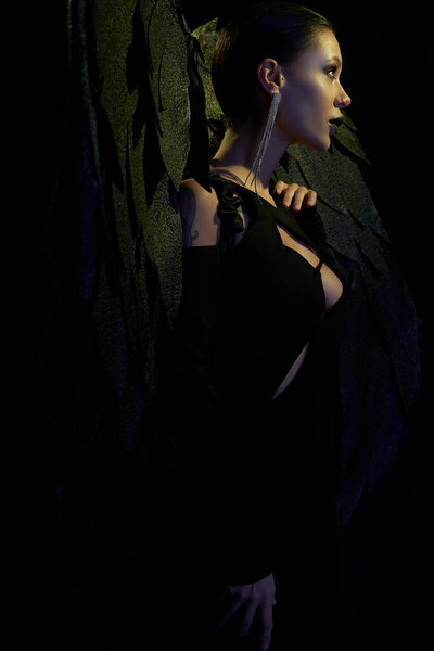 демоническое обаяние, вид сбоку на сексуальную женщину в Хэллоуинском костюме темного демона с крыльями на черном