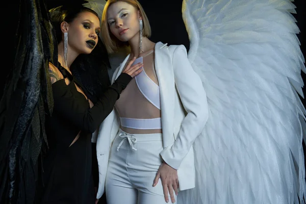 stock image women in costumes of dark demon and light angel with fantasy wings looking at camera on black