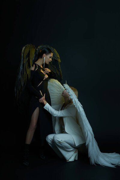 Ангел небесный, держась за руку черного демона, стоящего на черном фоне, женщины в костюмах на Хэллоуин