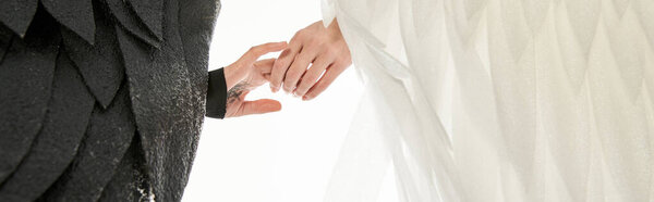 cropped view of angel and demon with black and light wings holding hands on white, banner