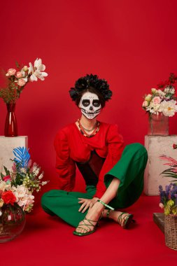 Catrina makyajlı kadın geleneksel dia de los muertos ofrenda 'nın yanında oturuyor kırmızıda çiçeklerle